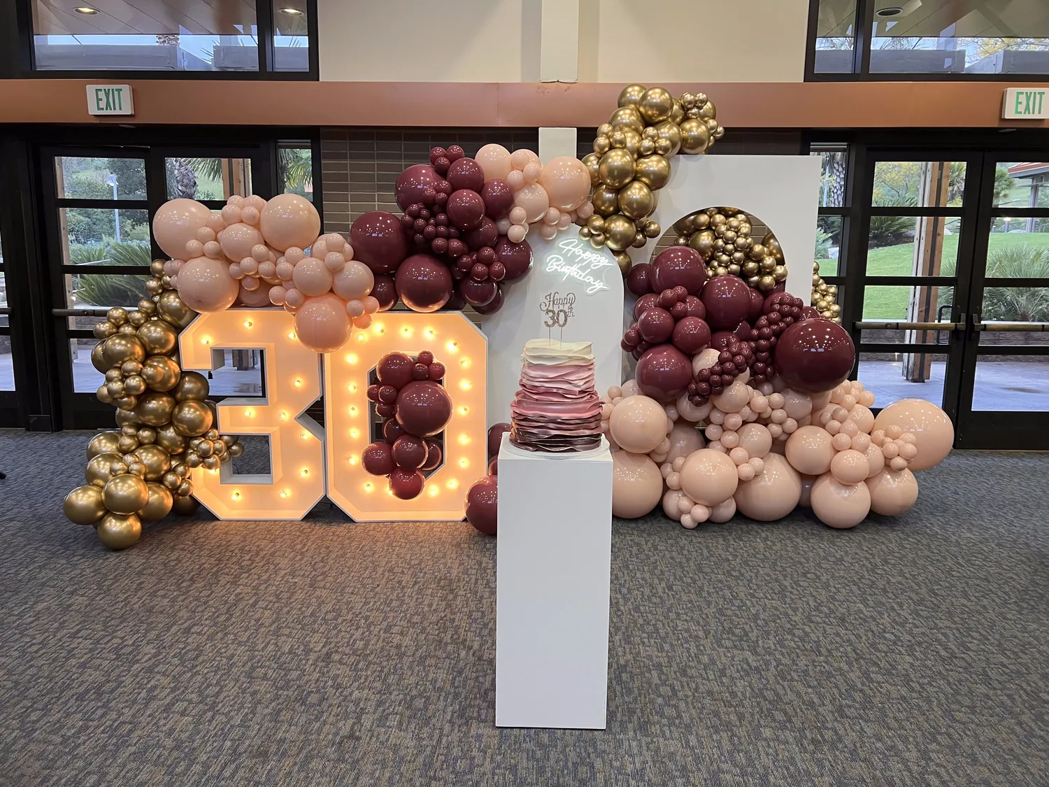 Light-up marquee 80 with burgundy, blush and gold balloon clusters in a venue.