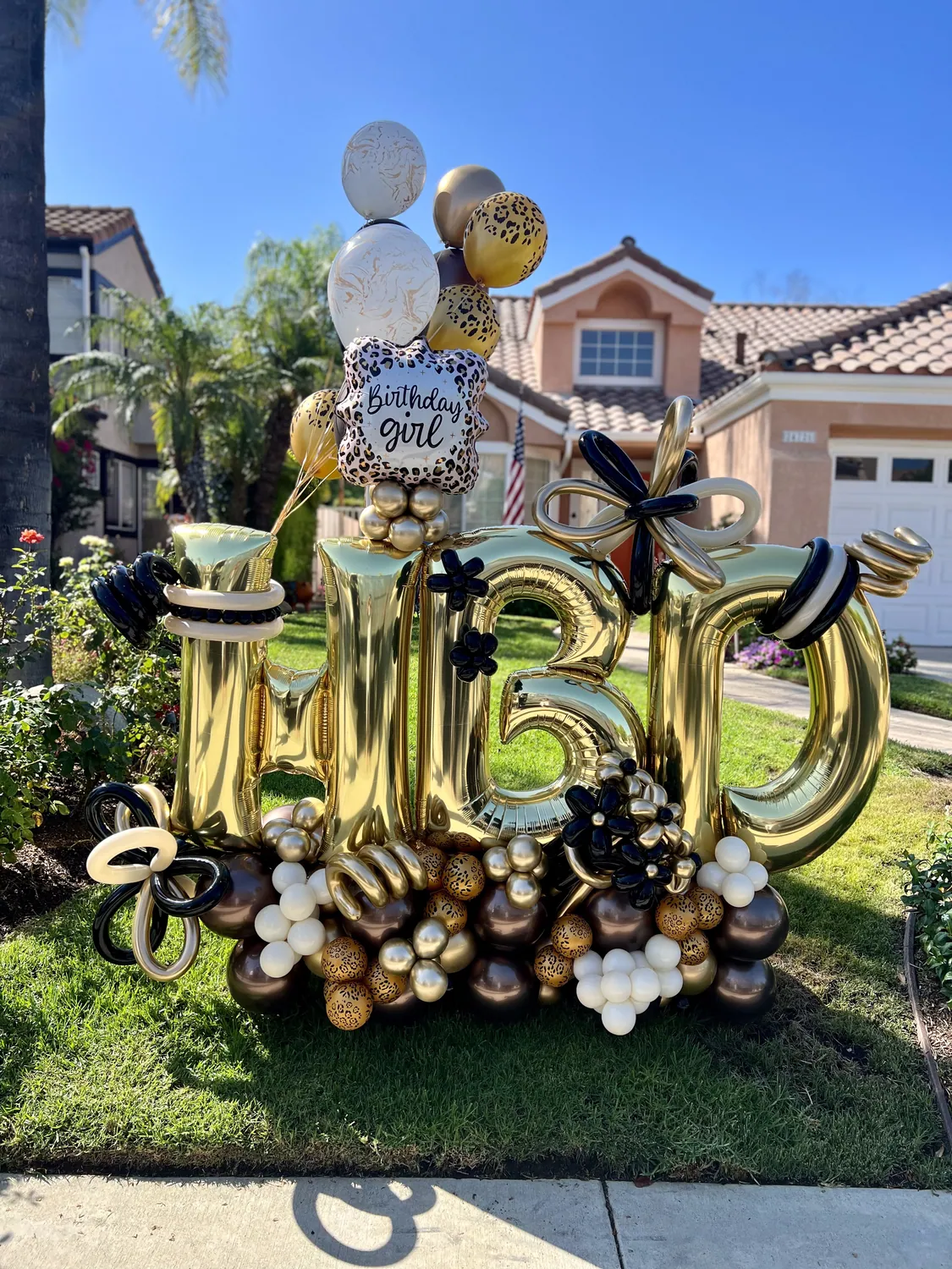 Balloon installation in peach, cream and coral with large paper flowers and a MOM sign, on a deck overlooking a lake at sunset.