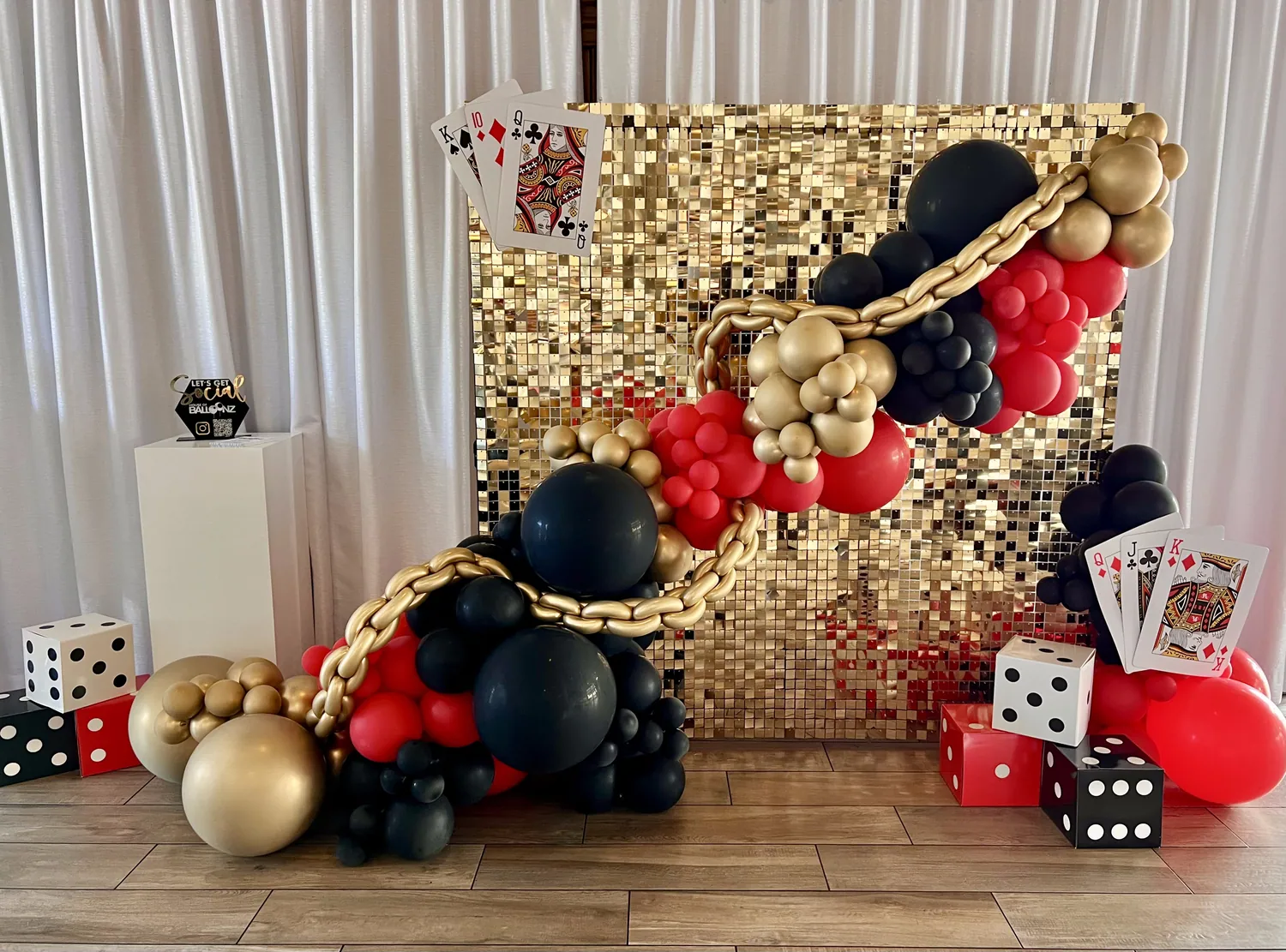 Casino night balloon installation in red, black and gold with playing cards and dice.