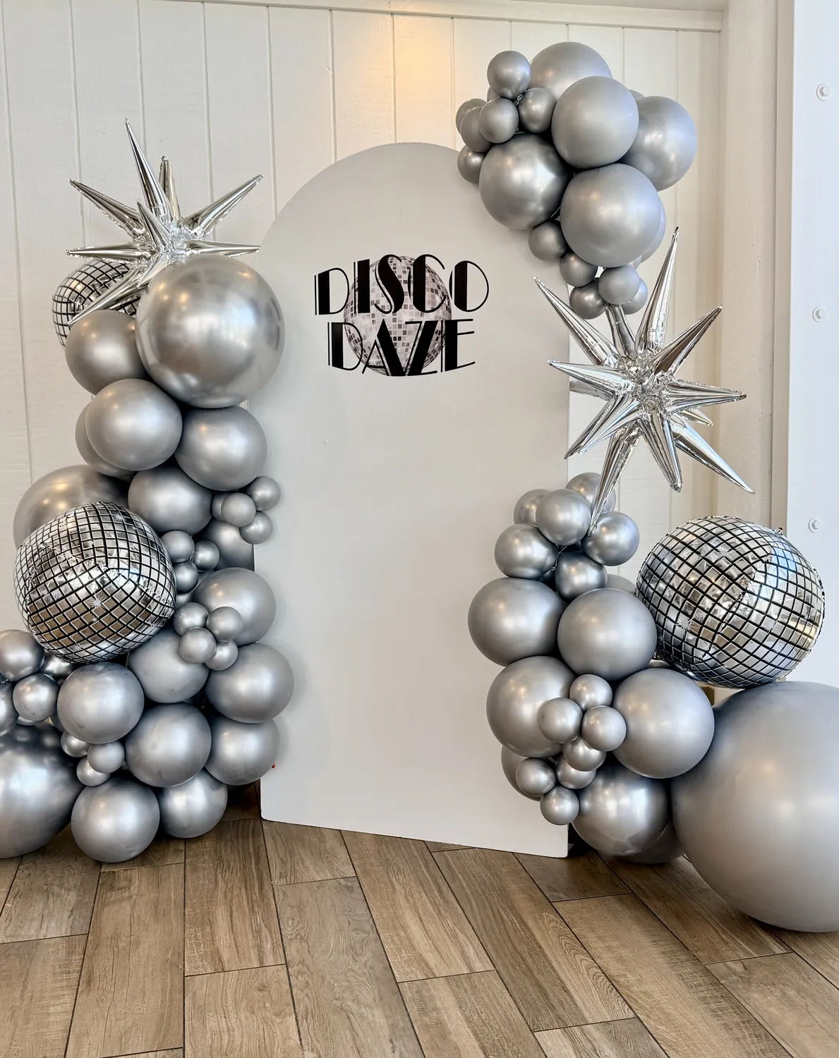 Silver chrome and disco ball balloon backdrop with foil starbursts.