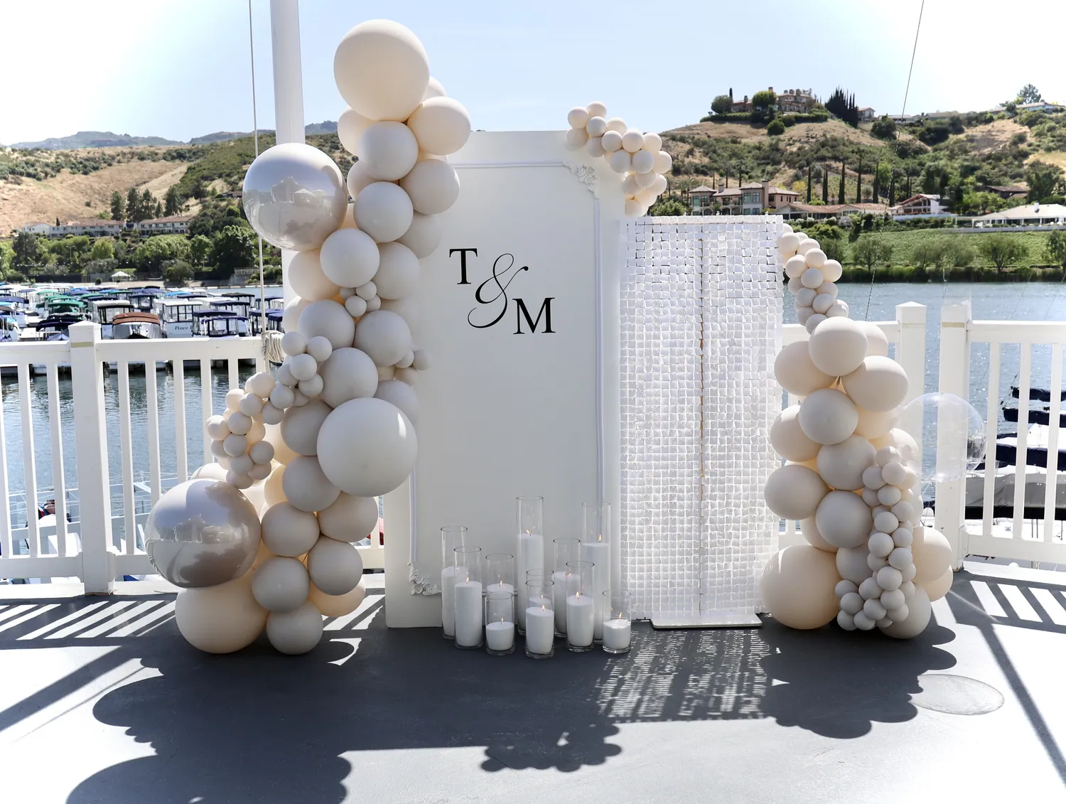 Ivory and sand balloon installation around a monogram panel on a terrace above a marina.