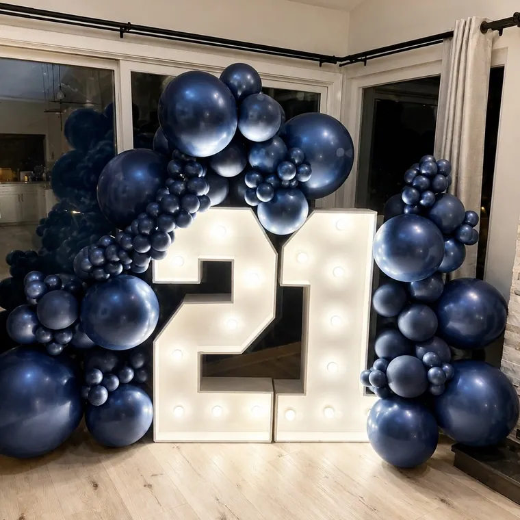 Light-up marquee number 21 framed by a navy and white balloon garland indoors.
