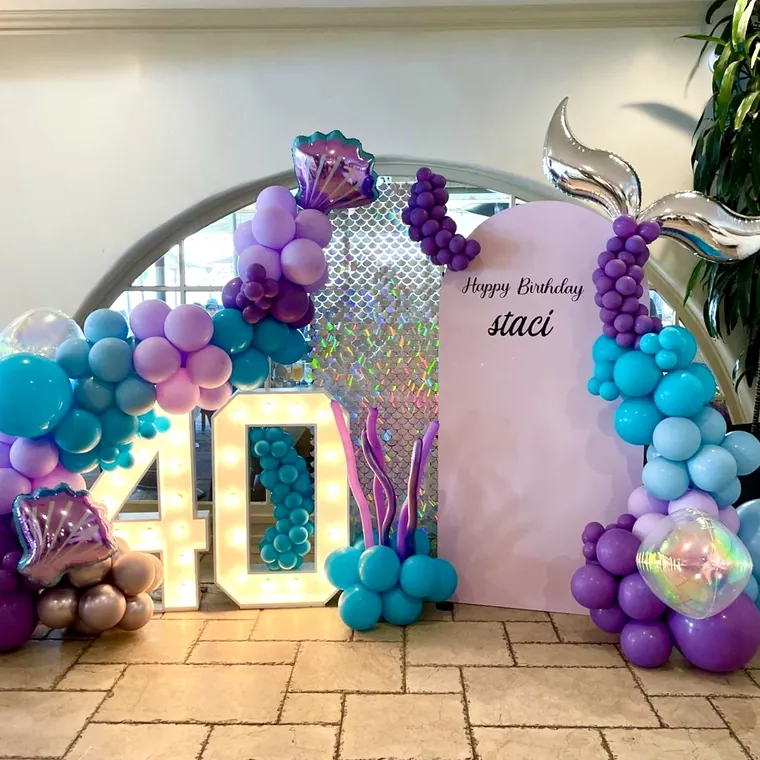Purple, teal and turquoise balloon backdrop with a mermaid tail against tall panels.