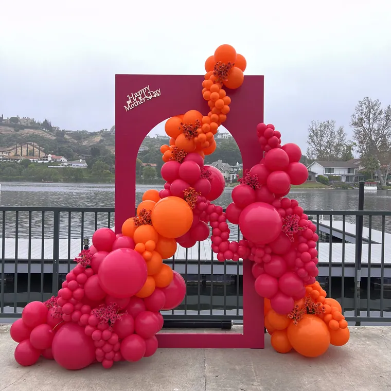 Hot pink and orange balloon backdrop on a terrace above a lake.