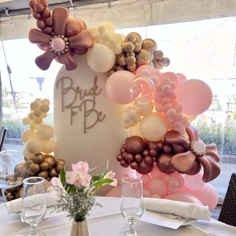 Blush and gold balloon flowers on a set table with glassware.