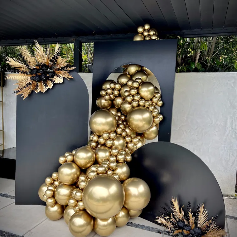 Gold chrome balloon installation on charcoal panels with bleached palm fans.
