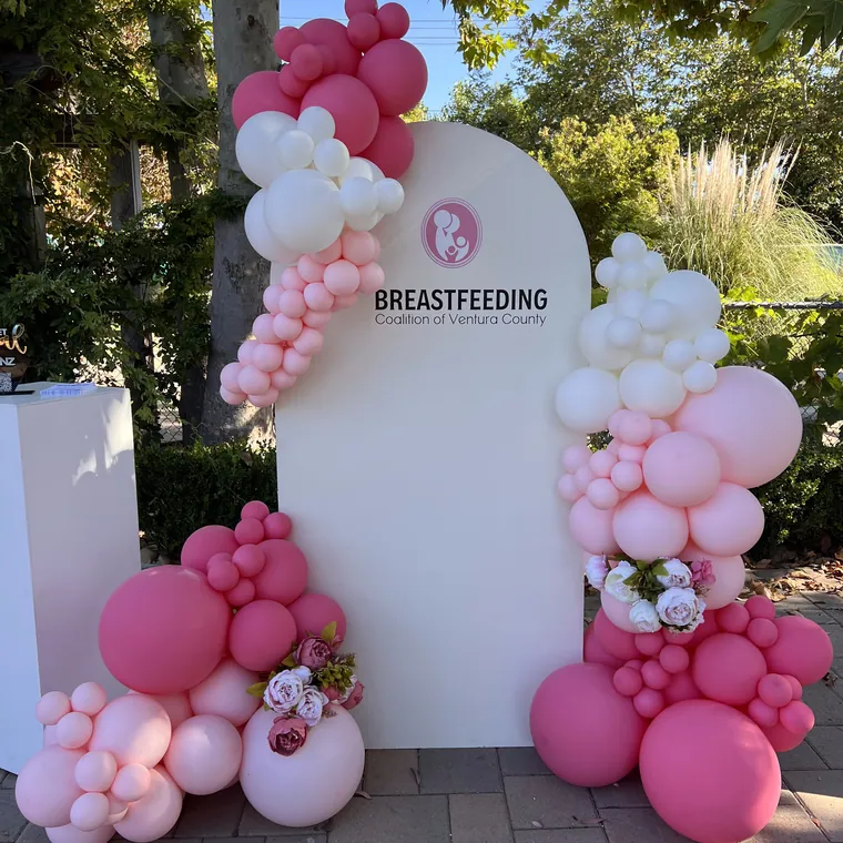 Pink and green balloon installation around a branded arched panel at a company event.