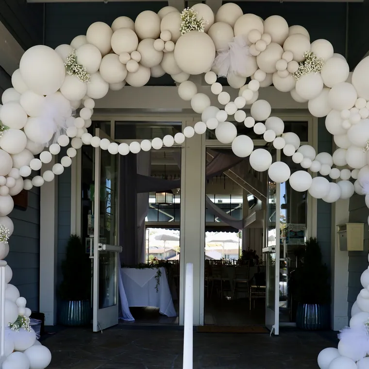 All-white balloon arch with pearl strands framing a doorway.