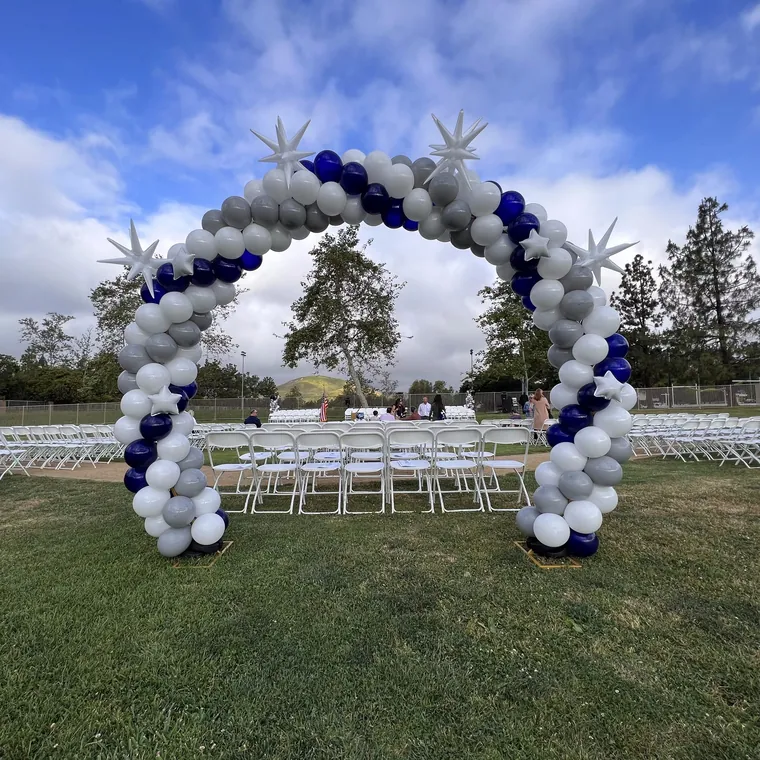 Large navy, silver and white balloon arch over rows of chairs on a lawn.