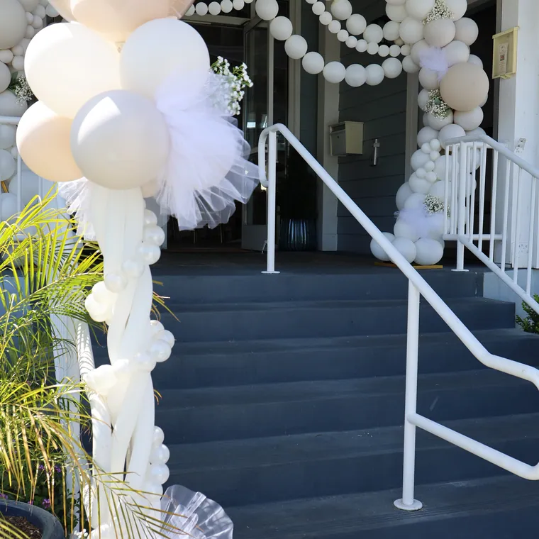 White balloon arch with pearl strands over a front staircase.