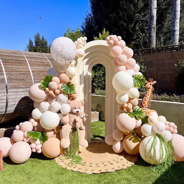 Safari themed balloon arch in greens and creams on a lawn.