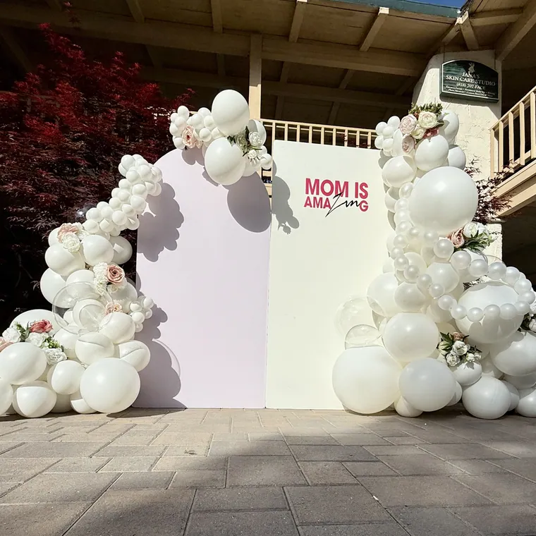 White balloon garland across two arched panels outdoors.
