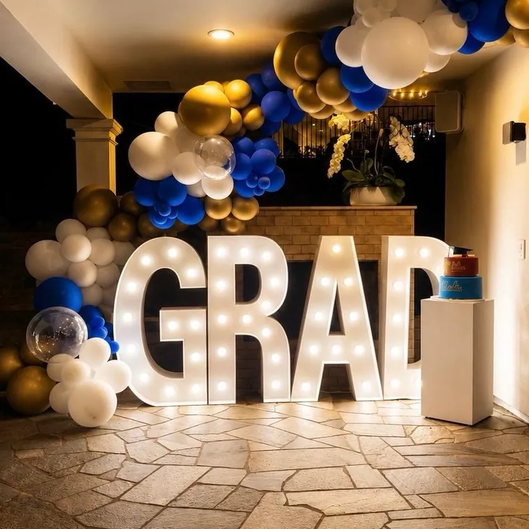 Light-up GRAD marquee letters under a navy and gold balloon garland.