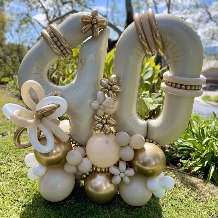 Cream and gold foil number 40 with balloon flowers on a lawn.