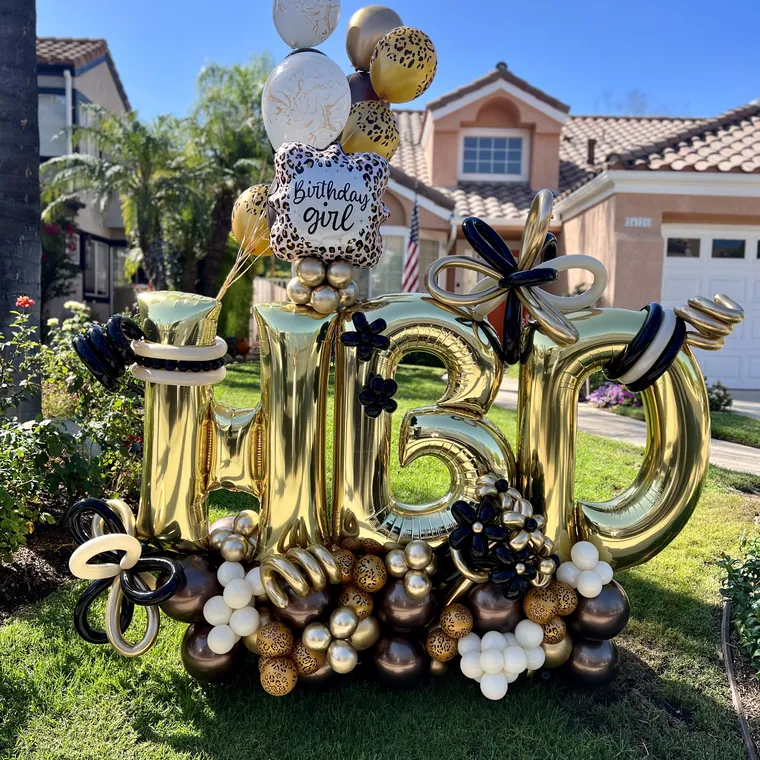 Giant gold foil 50 with black and gold balloons on a front lawn.