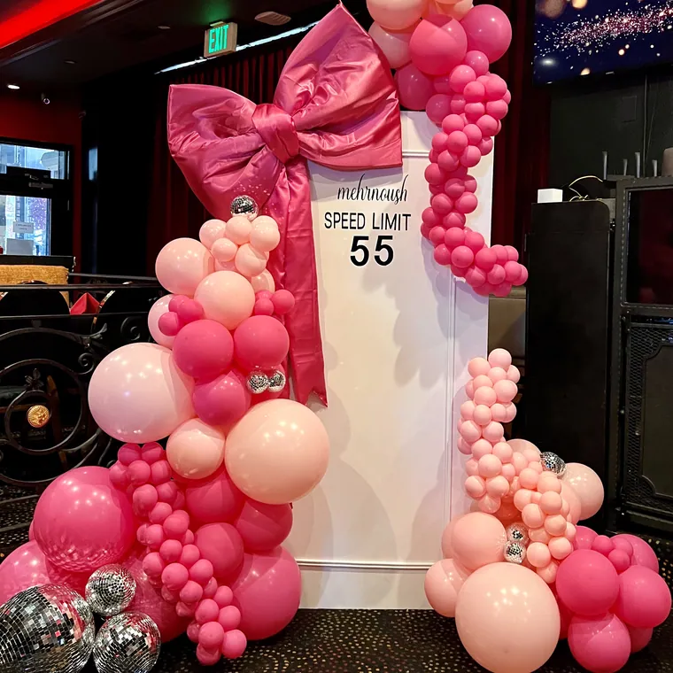 Oversized pink 55 speed-limit sign styled with a hot pink balloon garland and a fabric bow.
