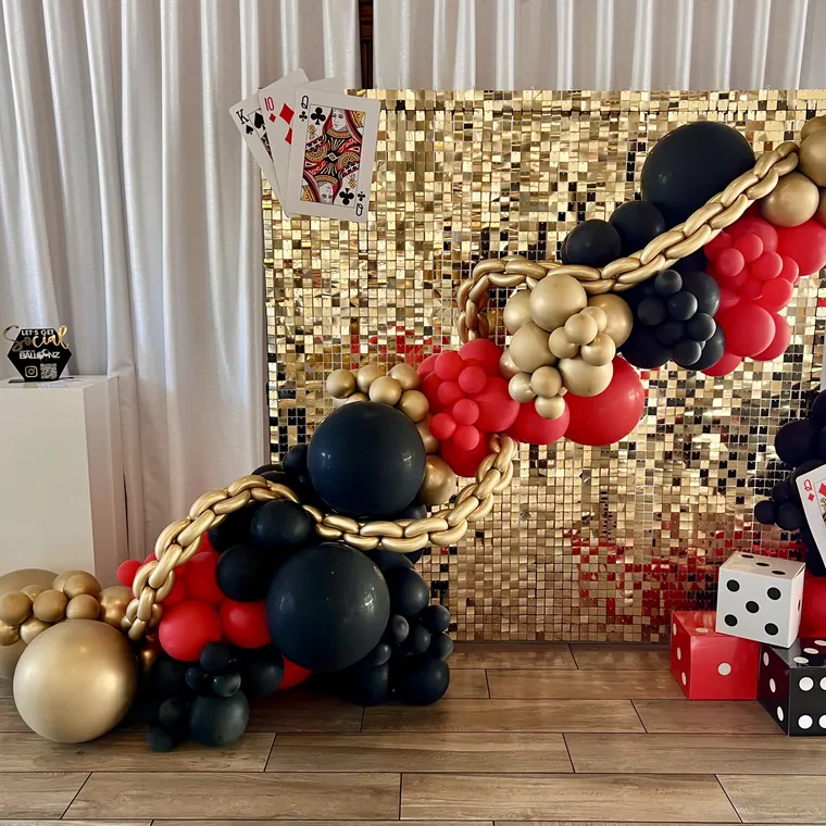 Casino night balloon installation in red, black and gold with cards and dice.