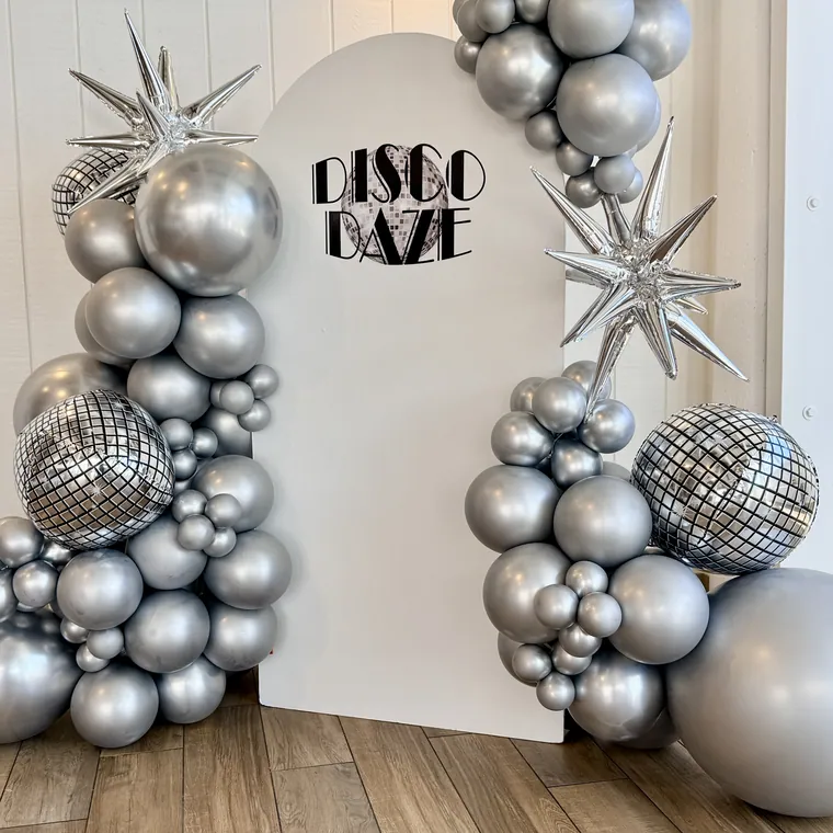 Silver chrome and disco ball balloon backdrop with foil starbursts.