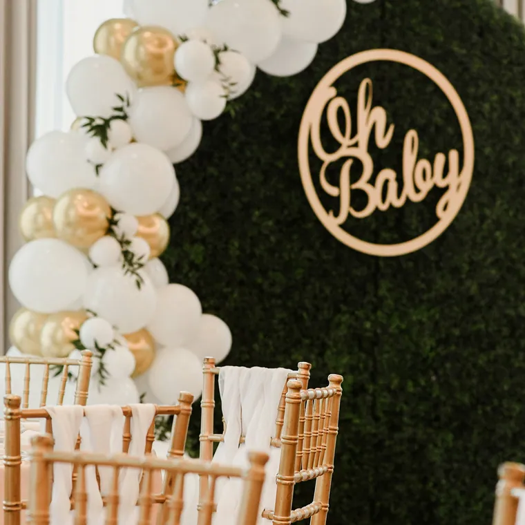 Cream and gold balloon arch against a hedge wall with an Oh Baby sign.