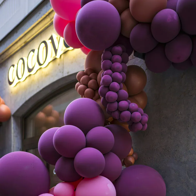 Purple and pink balloon installation framing a storefront sign.