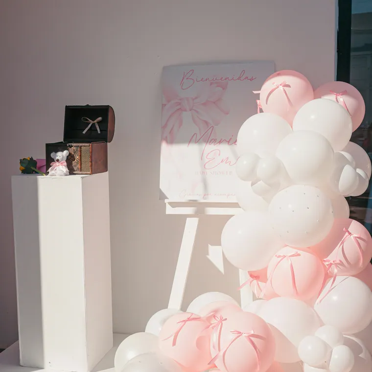 Blush and white balloon cluster beside a plinth at a small brand event.