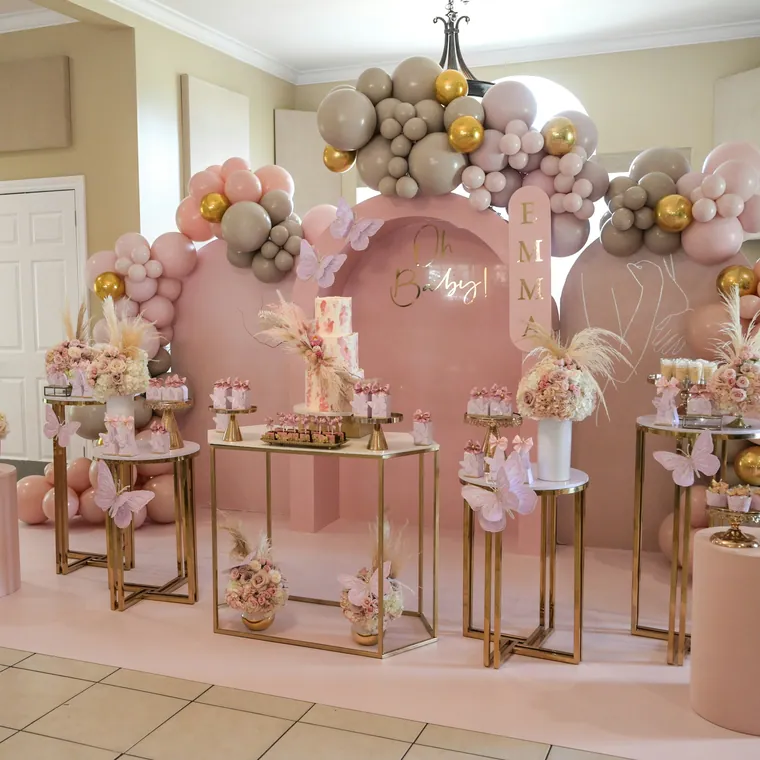 Blush and gold balloon arch behind a styled dessert and gift display.