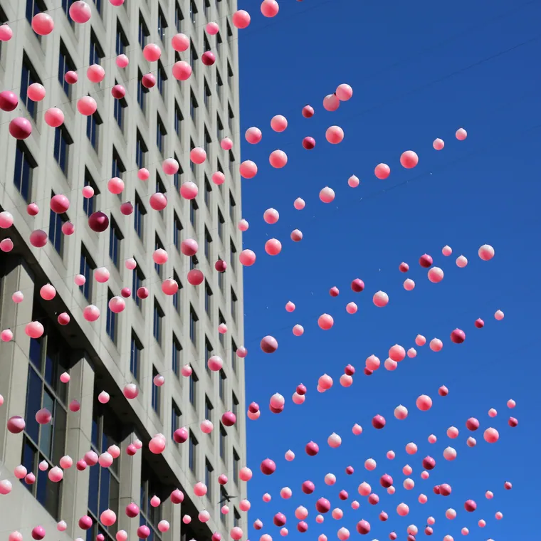 Pink balloons rising up the glass facade of an office building.