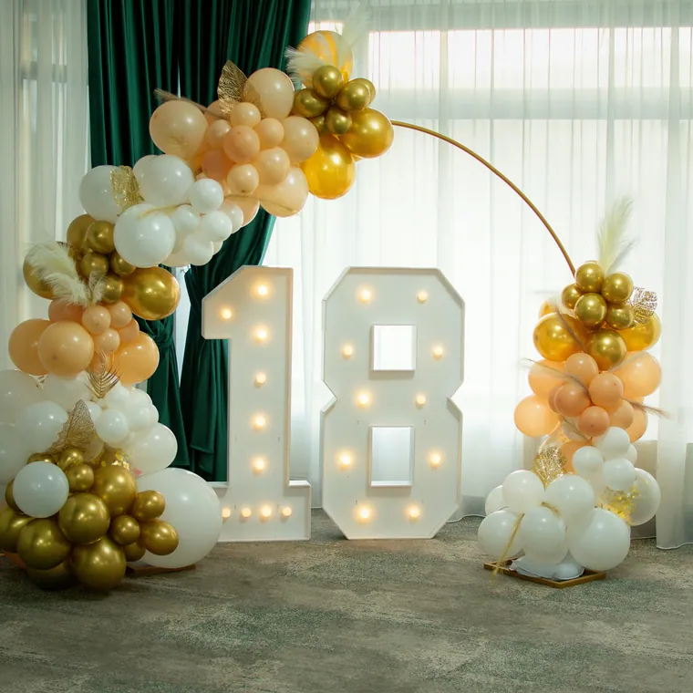 Light-up marquee 18 framed by a gold and cream balloon arch.