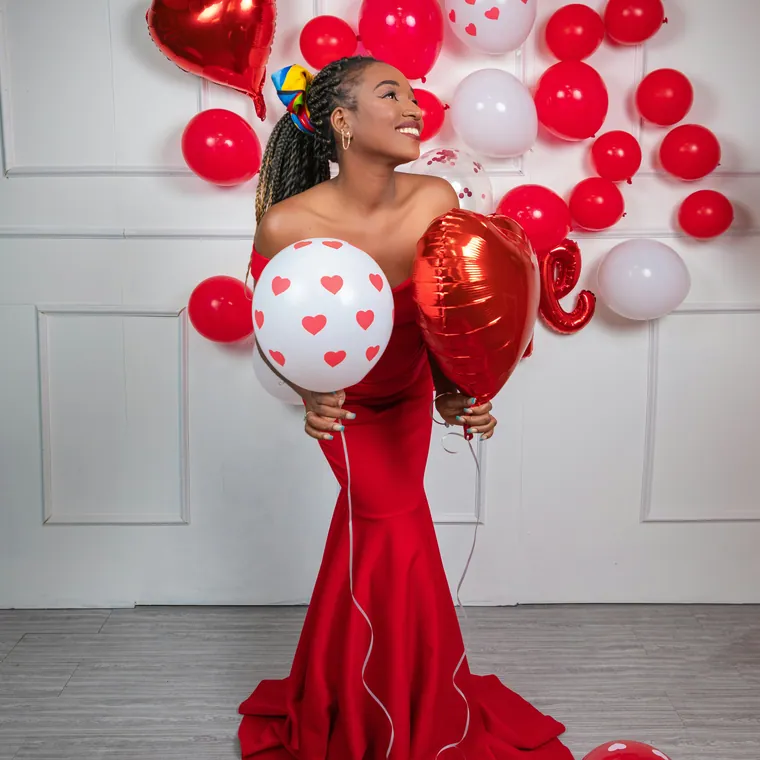 Studio set of red and white balloons with heart foils behind a seated subject.