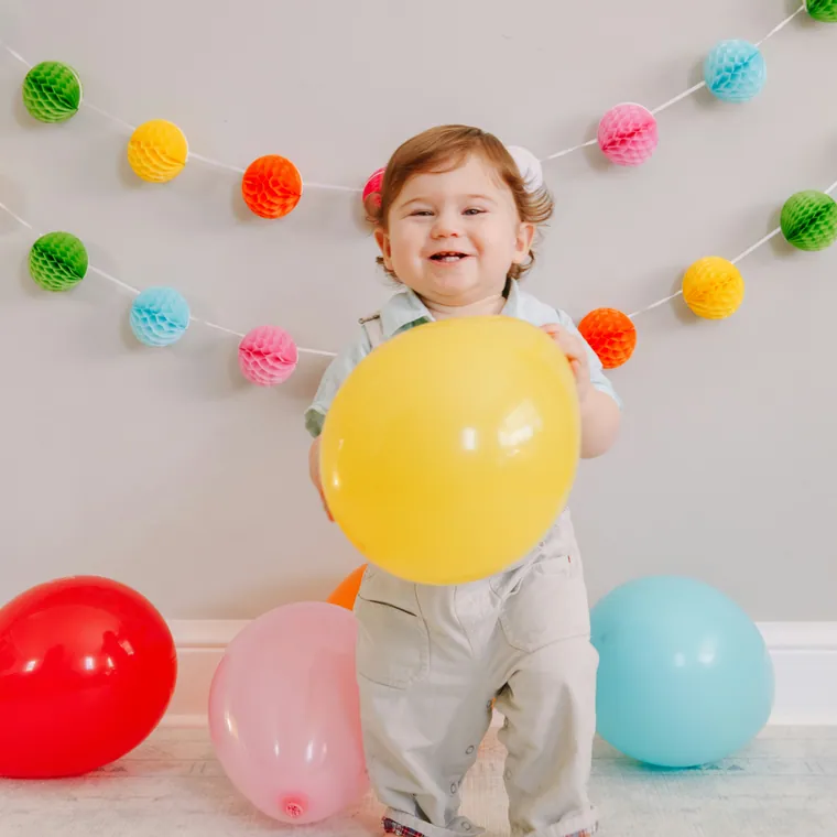 Toddler sitting among pastel balloons with a paper garland behind.
