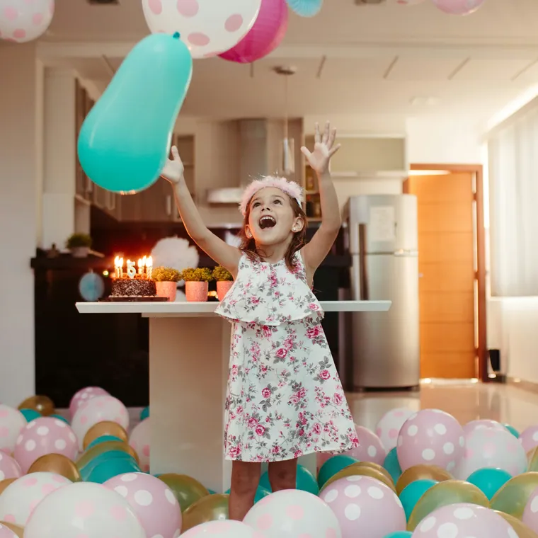 Child in a kitchen surrounded by pastel and polka dot floor balloons.