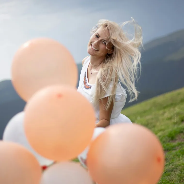 Woman outdoors behind a cluster of peach and cream balloons.