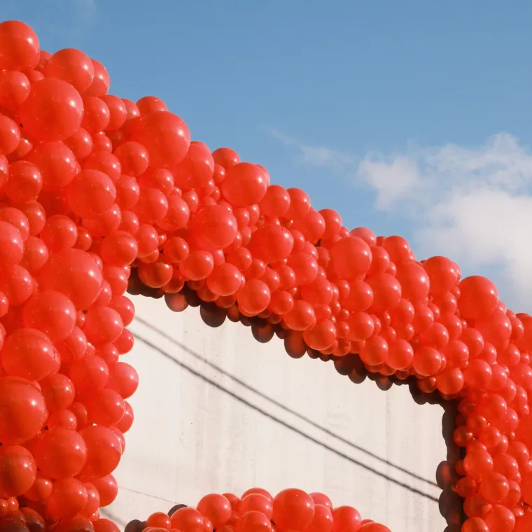Large outdoor wall of red balloons with a rectangular opening cut through it.