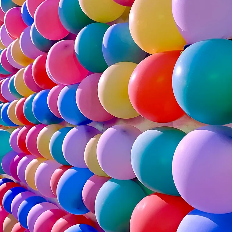 Wall of balloons in many bright colours packed edge to edge.